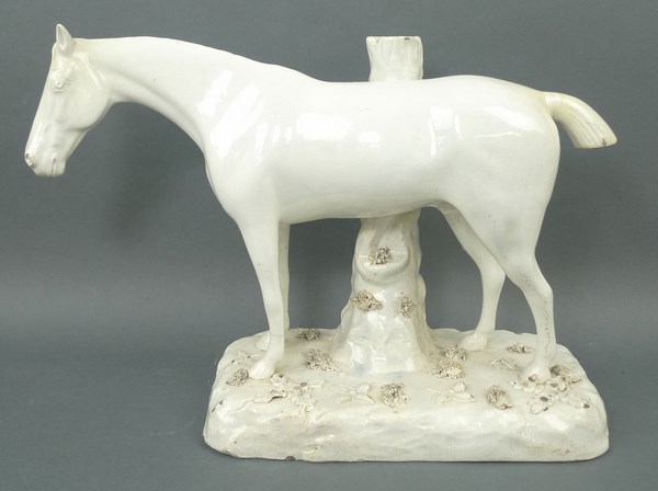 A stoneglazed figure of a horse, circa 1820, modelled standing against a tree stump, 34 by 13 by