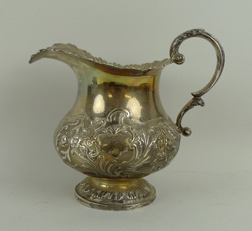 A William IV silver cream jug of baluster form embossed with leaf scrolls, flowers and shield