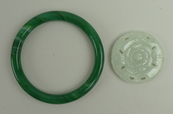 A Chinese green glass bangle, 8cm diameter, and a nephrite flower head medallion, 4.5cm diameter.