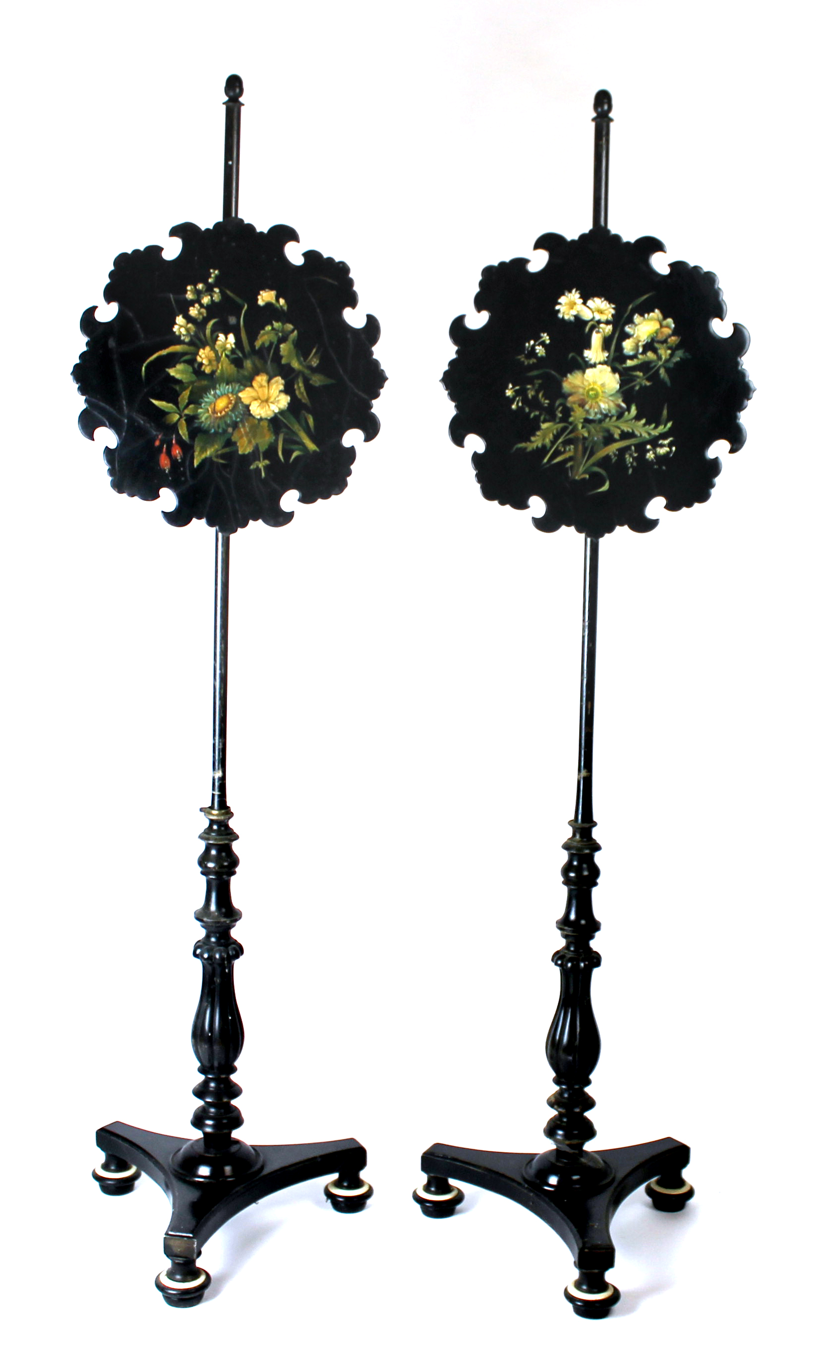 A pair of early 19th century ebonised pole screens, with floral painted lacquer panels on triform