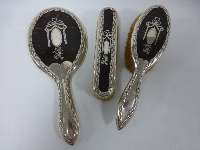 A George V silver and tortoiseshell three piece dressing table hand mirror and brush set, hallmarked