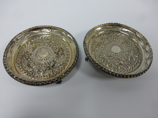 A pair of Victorian silver wine bottle coasters with embossed foliate decoration, on three