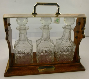 AN OAK AND EPNS MOUNTED TANTALUS having three lead crystal decanters and stoppers and an un-
