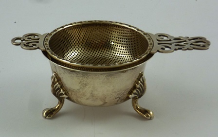 J.B. CHATTERLEY & SONS A SILVER TEA STRAINER with fretted handles, and BOWL en-suite, raised on