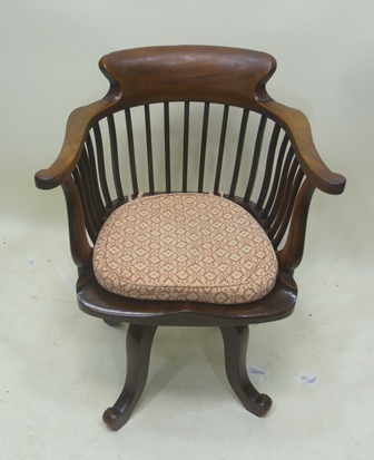 AN EDWARDIAN MAHOGANY REVOLVING DESK CHAIR having slatted back, twin swept arms, raised on a base