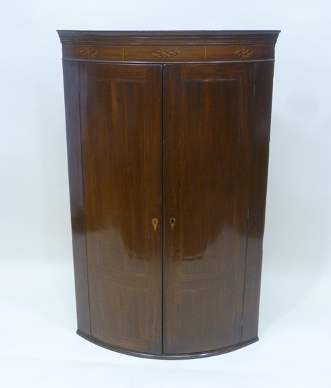 A LATE GEORGIAN MAHOGANY BOW FRONTED HANGING CORNER CUPBOARD having moulded pediment, triple floral