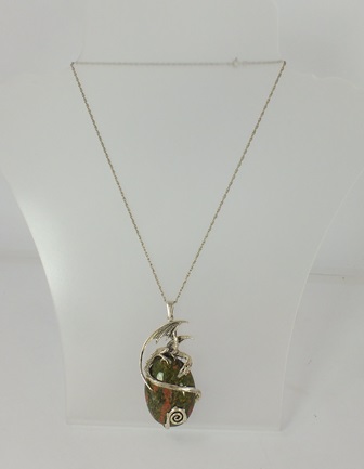 A SILVER COLOURED METAL PENDANT mounted with a dragon entwined around an oval cabochon serpentine