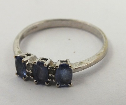 A RHODIUM FINISHED 14CT WHITE GOLD DRESS RING having three oval blue stones interset with four