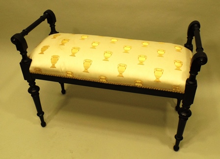 A VICTORIAN EBONISED DUET STOOL having twin ringed turned handles, gimped overstuffed seat, raised