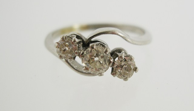 A DIAMOND THREE STONE CROSSOVER RING having cushion cut brilliants in platinum setting, ring size