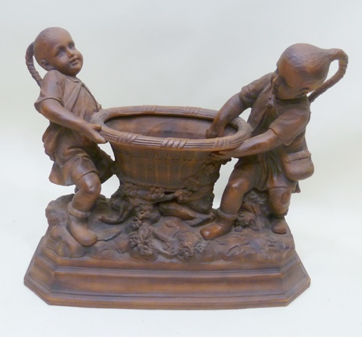 A 20TH CENTURY TERRACOTTA GROUP OF TWO PIG-TAILED BOYS holding a cistern on a naturalistic base,