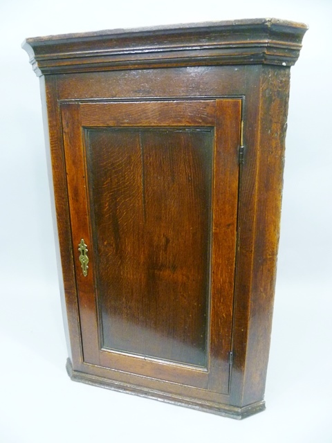 AN EARLY 19TH CENTURY OAK HANGING CORNER CUPBOARD having chamfered front, moulded pediment over a