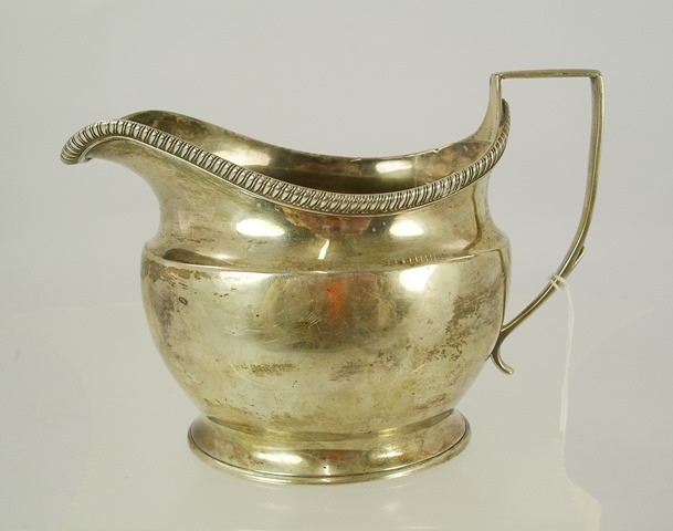 H** V** A GEORGE III SILVER MILK JUG, having gadroon applied wire rim oval belly with traces of