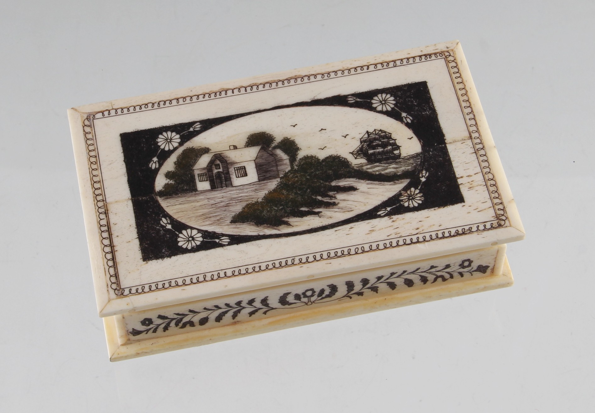 A reproduction scrimshaw style bone box, engraved with cottage with ship to background, restored,