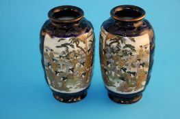 A pair of 20th century Japanese Satsuma vases on a dark blue field decorated with panels of figures,