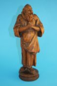 A carved wood figure of a monk with his hands clasped and holding a bag full of fruit. 40 cm high