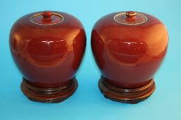 A pair of Chinese Sang de Boeuf vases of ovoid shape, each with circular lids and on wooden