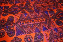 A roll of printed fabric on a red ground with geometric pattern in black, purple and orange.
