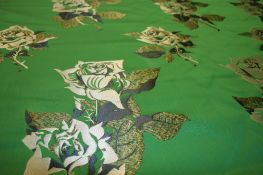 A roll of satin finish fabric on an emerald green ground and with woven roses of silver black and