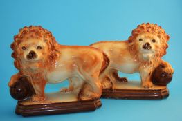 A pair of Victorian Staffordshire lions each with a paw raised on a ball, supported on stepped