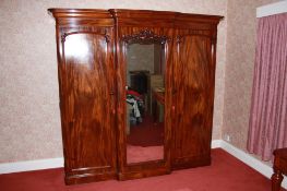 A Victorian mahogany triple door wardrobe with moulded cornice, the central mirrored door flanked