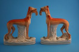 A pair of Victorian Staffordshire standing lurchers with rabbits in their mouths, supported on oval