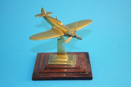 A small brass model of a spitfire, supported on a stepped mahogany base.12 cm long