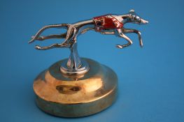A chrome plated car mascot in the form of a greyhound with red number 1 jacket, supported on a
