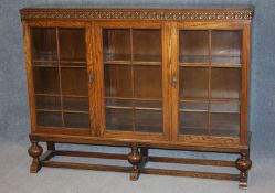 A Waring and Gillows Ltd oak three door glazed bookcase, supported on turned legs and plain uniting