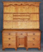 A large pine farmhouse dresser with delft rack below an arrangement of seven drawers and central