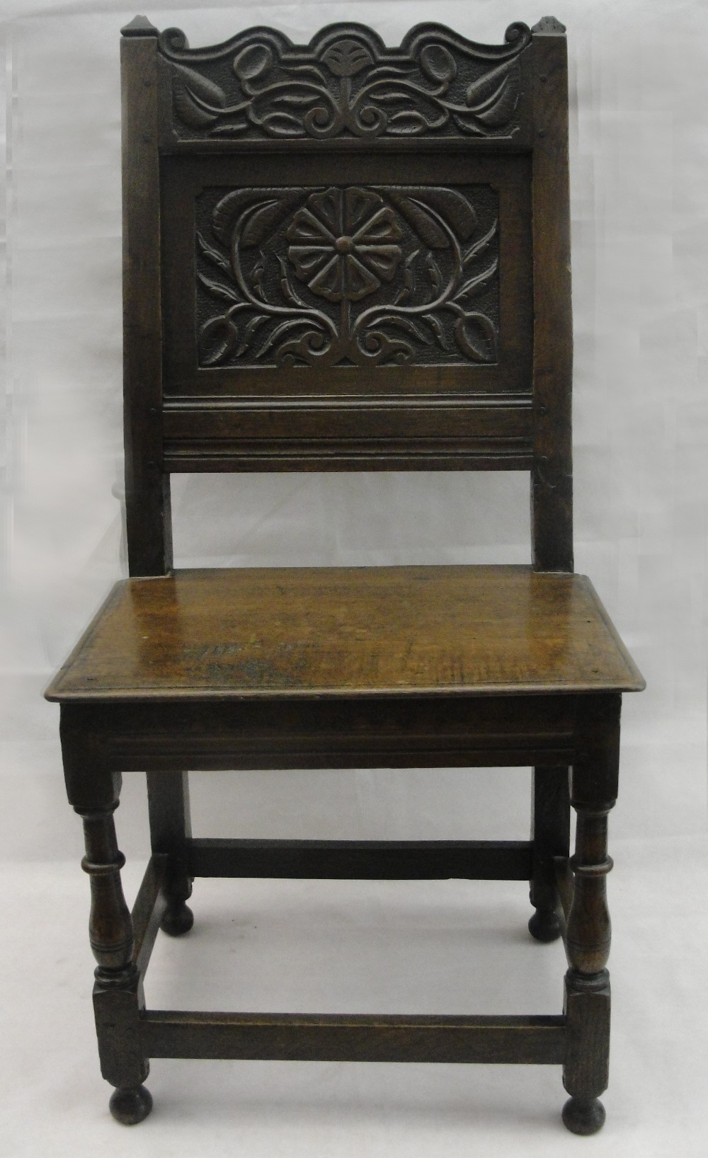 A 17th Century Oak Chair:
the shaped top rail above a panelled back carved with a thistle, on turned