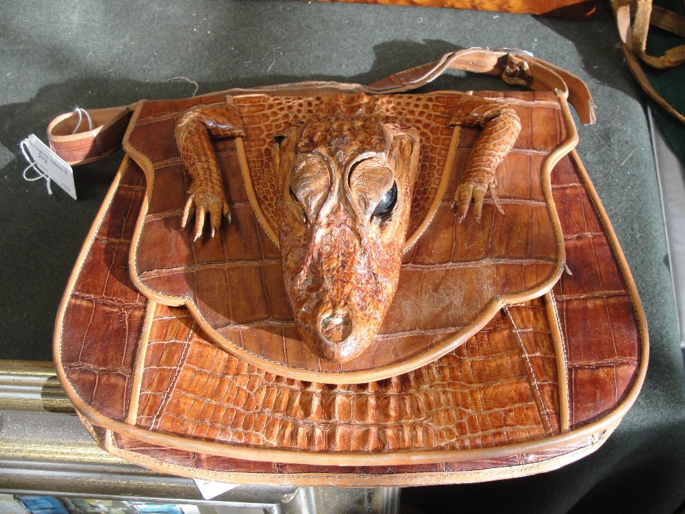 A tan leather crocodile saddle-style handbag with the head and front feet on the flap