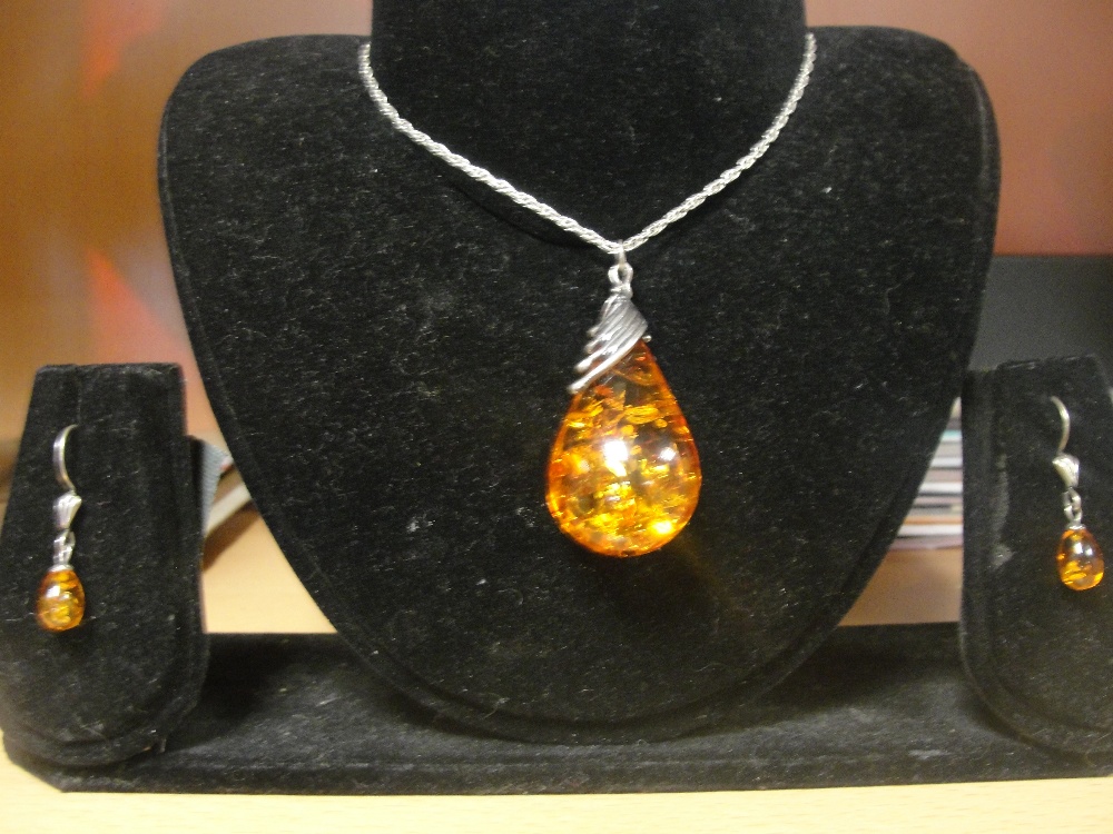 A large amber drop pendant with matching earrings in a silver mount