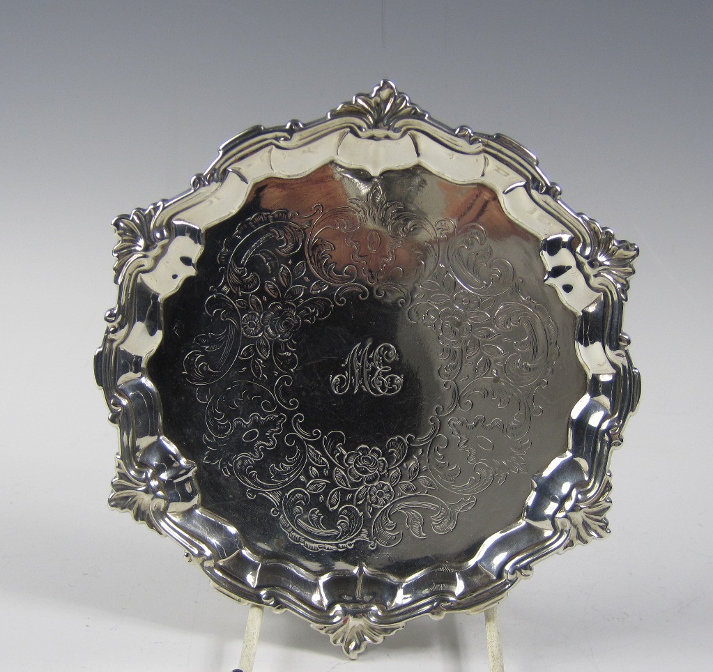 A George II shaped circular silver Waiter with floral and leafage scroll engraving, raised on hoof