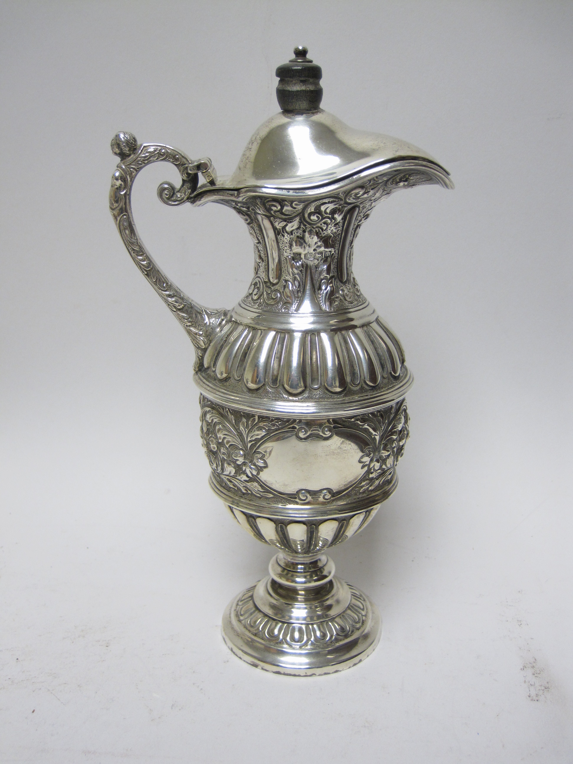 A George V silver Claret Jug with floral and scroll embossing, vacant cartouche, mask and scroll