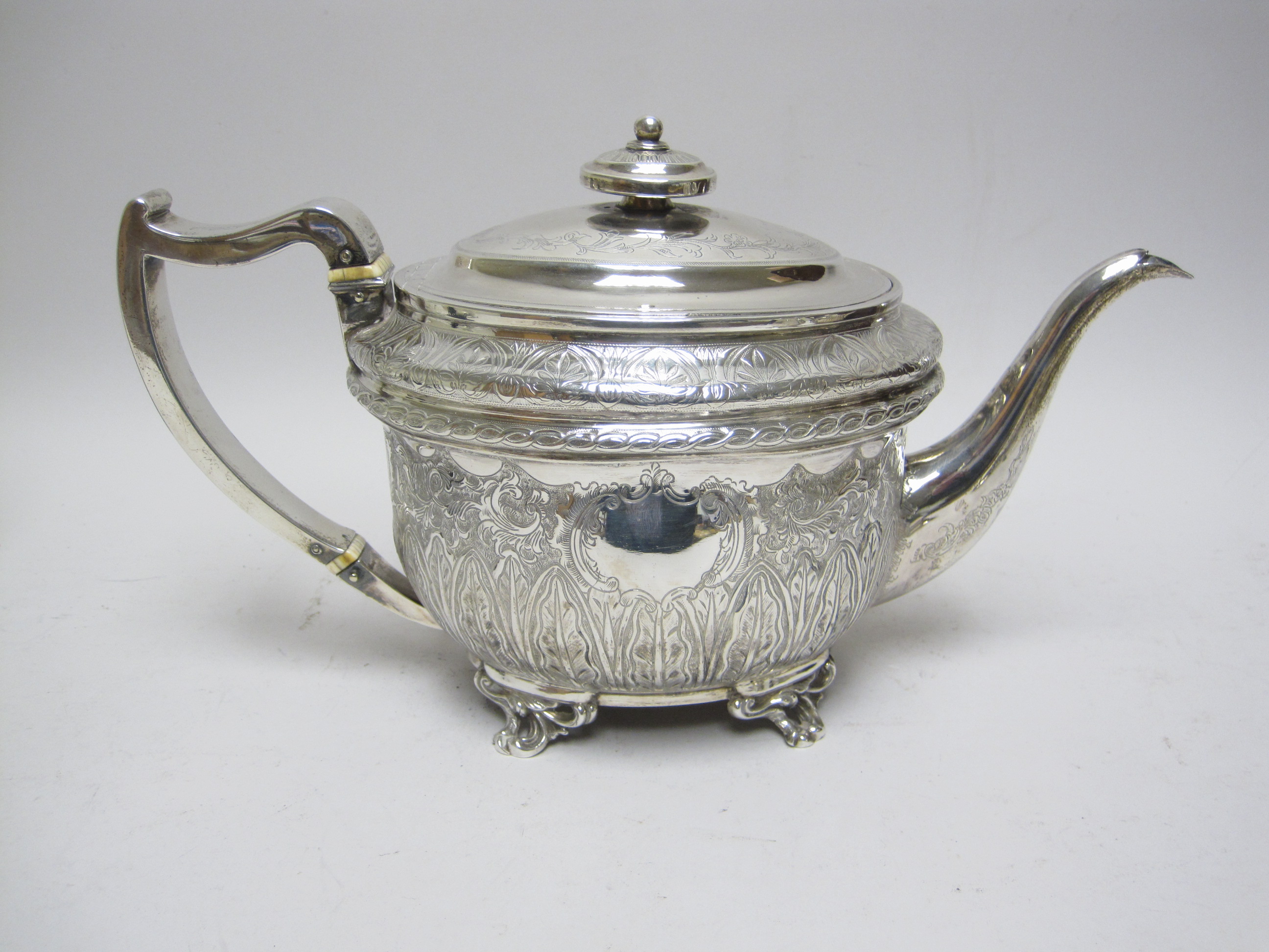 A George III silver oval Teapot with leafage engraved frieze and vacant cartouche on three leafage