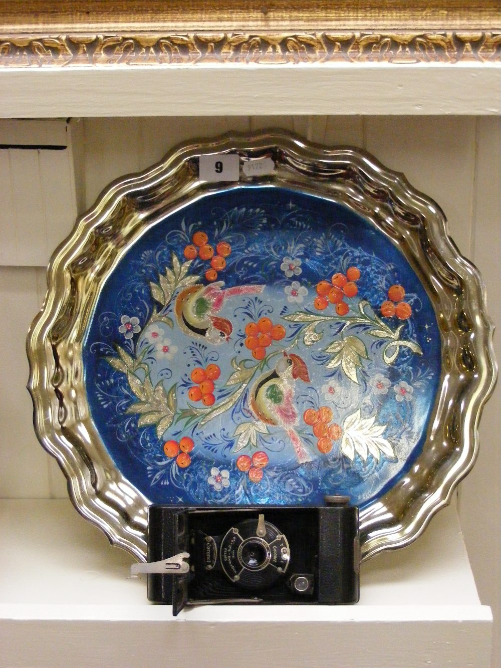 A vintage Coronet bellows camera and a painted metal circular tray decorated with birds.