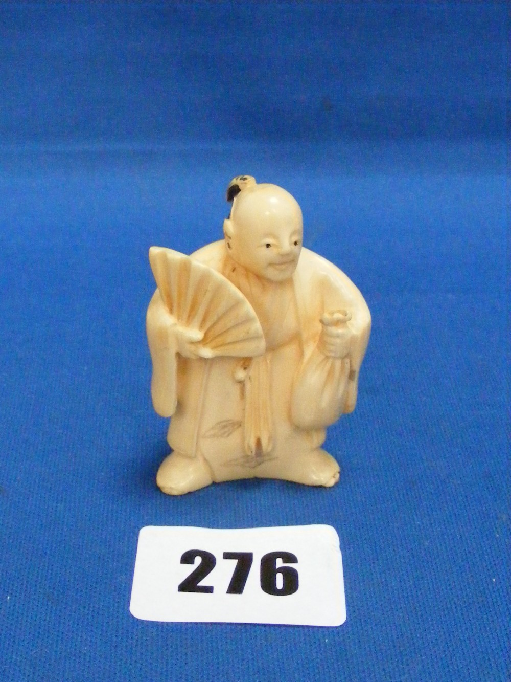 An ivory netsuke figure of an elder wearing robes, his black hair tied back in a bow, holding a