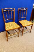 A pair of Edwardian bedroom chairs having spindle backs and cane seats (2)