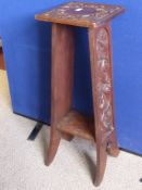 An Arts & Crafts mahogany torchere having carved decoration to the top, sides and under shelf,