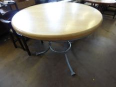 Circular oak kitchen table on a shaped metal base having three splayed feet, the supports having