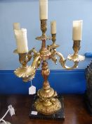 A four branch ornate gilded metal table lamp, masks to the edge of the base, the lamp supported on