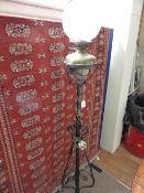 A wrought iron converted oil lamp with original glass shade and funnel, approximately 170 cms high.