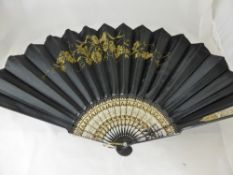 An Edwardian black satin mourning fan having gold embroidery depicting grape vines and a bow with