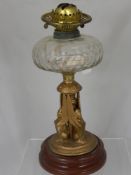 A vintage oil lamp with cut glass bowl, supported on a gilded centre column with three figures,