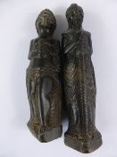 Two ancient dark green carved stone figures depicting a man and a woman, the bearded man carved