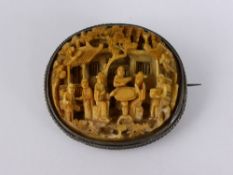 A hand carved antique Chinese ivory brooch depicting characters outside a dwelling in silver metal