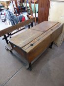 A vintage double school desk with seat attached, each part of the desk having an inkwell hole and