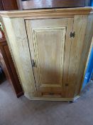 A vintage pine corner cupboard having a panelled door with small drawer below, the interior having