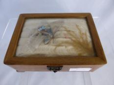 A jewellery box decorated with silk and a butterfly beneath a glass lid.